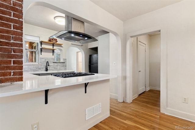 521 Harrison St, Denver, CO 80206 - kitchen with island range hood, black appliances, arched walkways, light wood-style flooring, and a kitchen bar