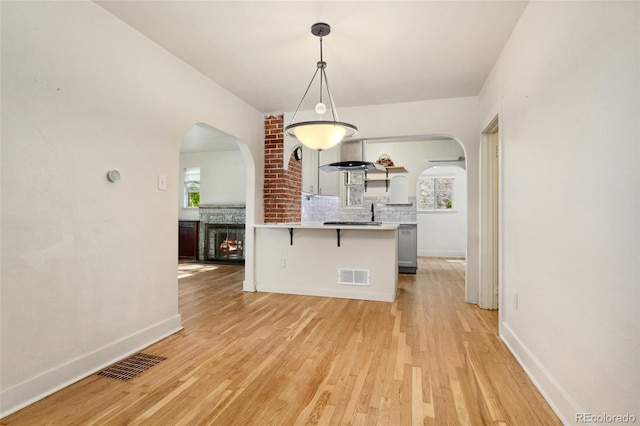521 Harrison St, Denver, CO 80206 - kitchen featuring backsplash, a breakfast bar area, arched walkways, light wood-type flooring, and a multi sided fireplace