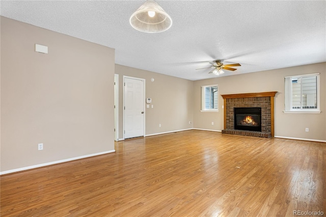 unfurnished living room featuring ceiling fan, a brick fireplace, a textured ceiling, and light hardwood / wood-style flooring