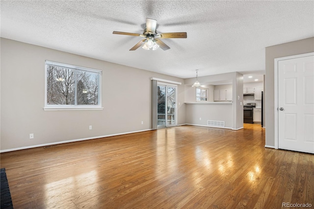 unfurnished living room with hardwood / wood-style flooring, ceiling fan, plenty of natural light, and a textured ceiling