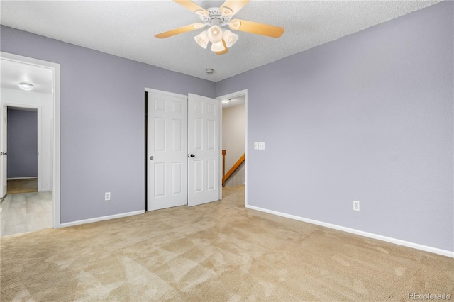 unfurnished bedroom with a textured ceiling, light colored carpet, a closet, and ceiling fan