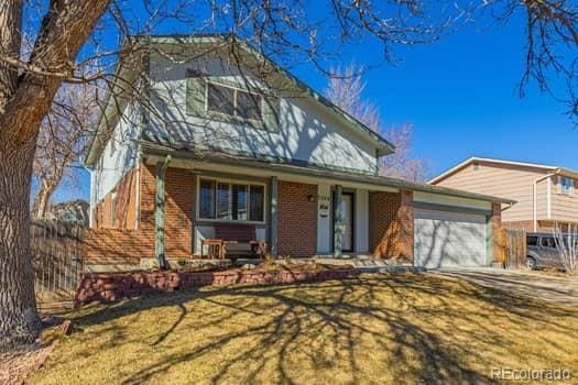 traditional-style home featuring brick siding, a porch, an attached garage, a front yard, and fence