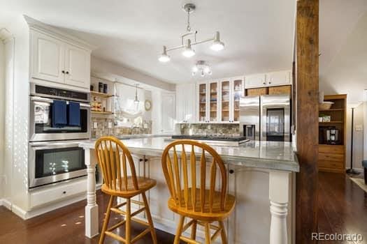 kitchen with dark wood-style flooring, appliances with stainless steel finishes, glass insert cabinets, white cabinets, and a kitchen island