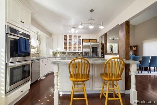 kitchen featuring a breakfast bar area, stainless steel appliances, white cabinetry, dark wood-style floors, and glass insert cabinets