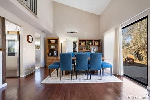 dining room with high vaulted ceiling, wood finished floors, stacked washer and clothes dryer, and a healthy amount of sunlight