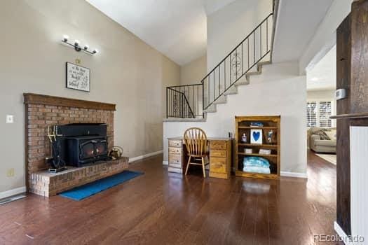 interior space with lofted ceiling, wood finished floors, a wood stove, and baseboards