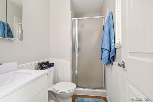 bathroom featuring toilet, a wainscoted wall, a shower stall, and vanity