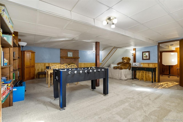 recreation room featuring a wainscoted wall, wooden walls, carpet flooring, and a drop ceiling