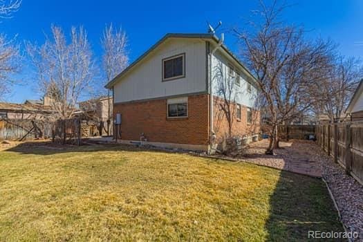 back of property featuring a fenced backyard, a lawn, and brick siding