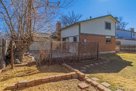 back of property featuring a fenced backyard, a chimney, a lawn, and brick siding