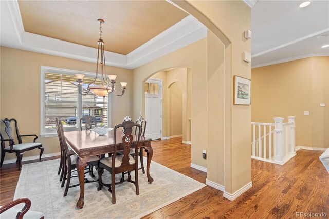 10182 Bristleridge St, Parker, CO 80134 - dining room featuring arched walkways, wood finished floors, a chandelier, ornamental molding, and a raised ceiling