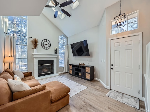 living room featuring a wealth of natural light, light hardwood / wood-style flooring, high vaulted ceiling, and ceiling fan with notable chandelier