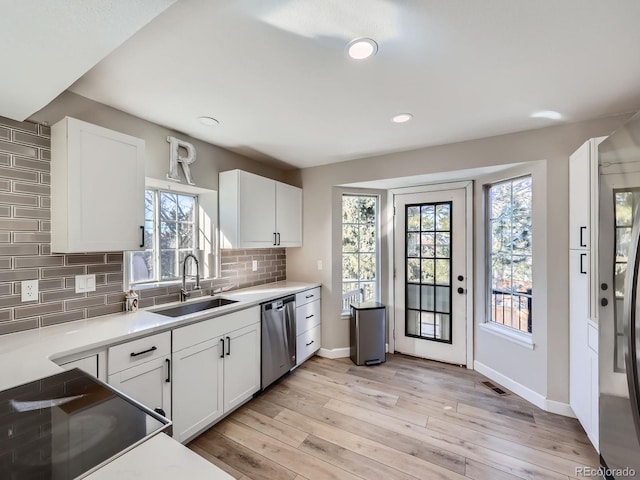 kitchen with backsplash, stainless steel dishwasher, sink, light hardwood / wood-style floors, and white cabinetry