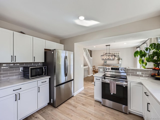 kitchen featuring white cabinets, hanging light fixtures, decorative backsplash, appliances with stainless steel finishes, and light hardwood / wood-style floors