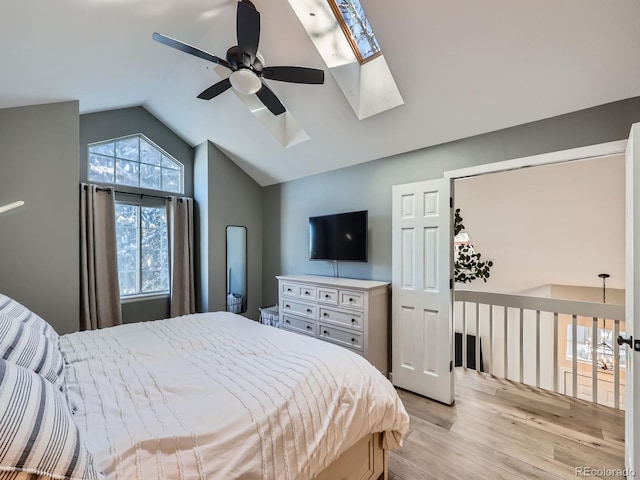 bedroom featuring ceiling fan, light wood-type flooring, and lofted ceiling with skylight