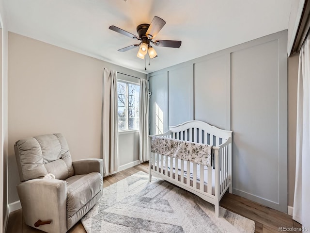 bedroom featuring ceiling fan, light wood-type flooring, and a crib