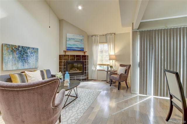 sitting room with a tiled fireplace, light hardwood / wood-style floors, and vaulted ceiling