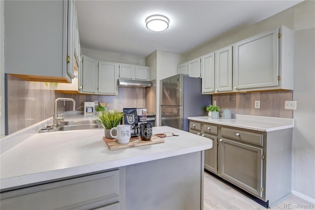 kitchen with light wood-type flooring, stainless steel refrigerator, gray cabinetry, and sink