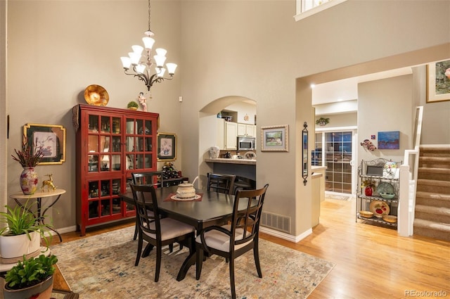 dining room featuring an inviting chandelier, a towering ceiling, and light wood-type flooring