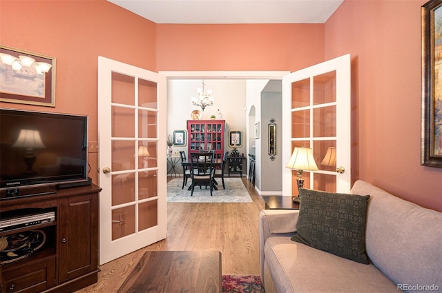 living room featuring an inviting chandelier, light hardwood / wood-style floors, and french doors