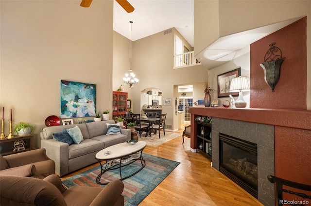 living room with hardwood / wood-style floors, a towering ceiling, ceiling fan with notable chandelier, and a tile fireplace