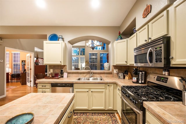 kitchen with tile countertops, sink, cream cabinetry, stainless steel appliances, and light hardwood / wood-style flooring