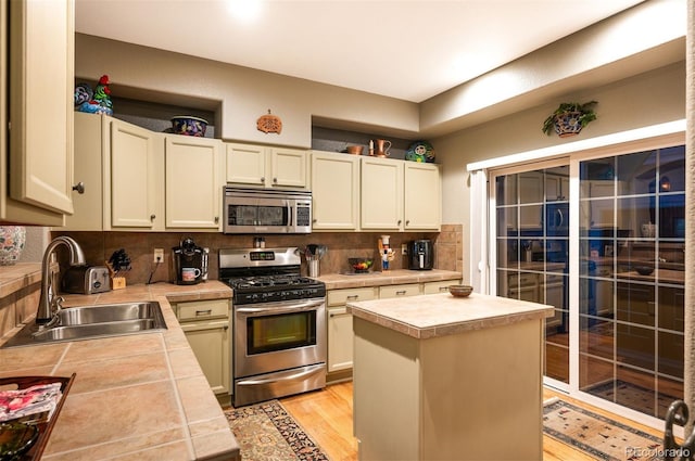 kitchen with appliances with stainless steel finishes, tasteful backsplash, sink, a center island, and light hardwood / wood-style flooring