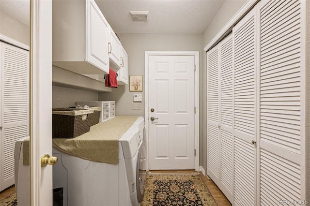 clothes washing area featuring a textured ceiling, light hardwood / wood-style floors, cabinets, and washing machine and clothes dryer