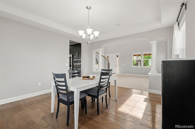 7606 S Valleyhead Ct, Aurora, CO 80016 - dining area featuring arched walkways, a tray ceiling, decorative columns, and wood finished floors