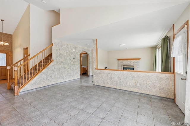 6510 Packsaddle Ct, Colorado Springs, CO 80922 - unfurnished living room with stairway, high vaulted ceiling, a brick fireplace, arched walkways, and tile patterned flooring
