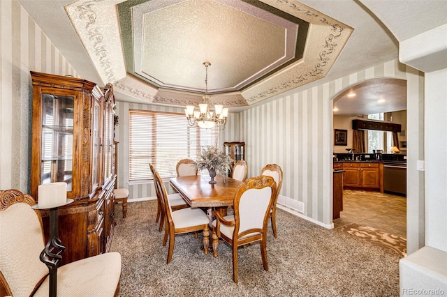 carpeted dining space featuring a raised ceiling, ornamental molding, a healthy amount of sunlight, and an inviting chandelier