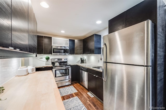 kitchen featuring tasteful backsplash, light stone countertops, dark hardwood / wood-style flooring, and stainless steel appliances