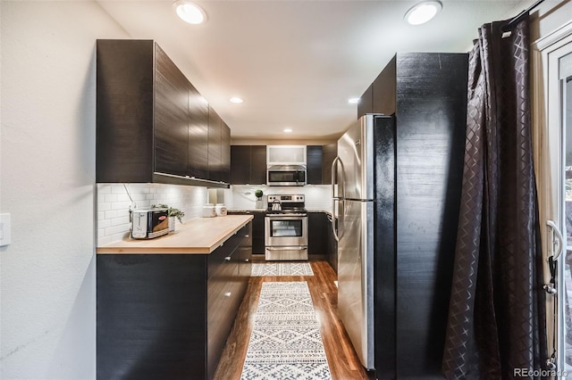 kitchen with light wood-type flooring, stainless steel appliances, tasteful backsplash, and butcher block countertops