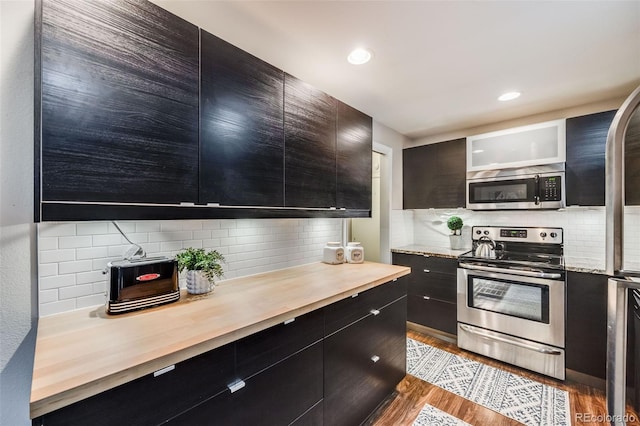 kitchen featuring light stone countertops, backsplash, appliances with stainless steel finishes, and light hardwood / wood-style flooring