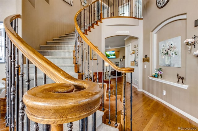 staircase featuring baseboards, arched walkways, a high ceiling, and wood finished floors