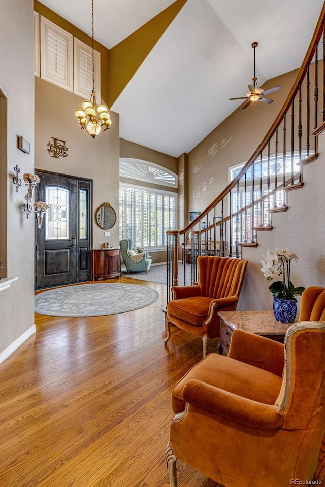 entryway with ceiling fan with notable chandelier, a towering ceiling, stairway, wood finished floors, and baseboards