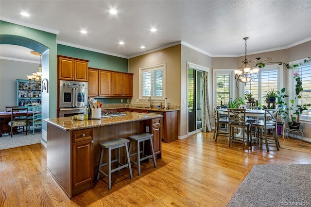 kitchen with light wood-style floors, an inviting chandelier, a kitchen island, brown cabinets, and baseboards