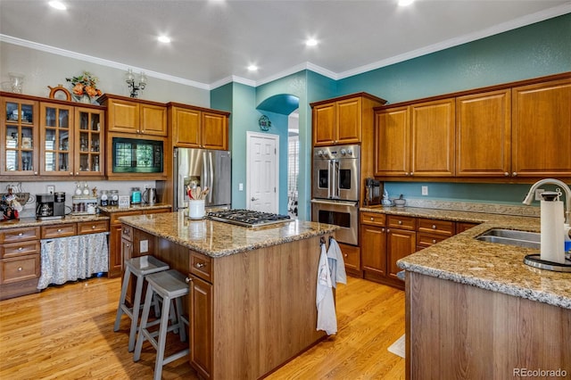 kitchen with light stone counters, crown molding, brown cabinets, stainless steel appliances, and a sink