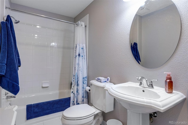 full bath featuring toilet, a textured wall, a sink, and shower / tub combo with curtain