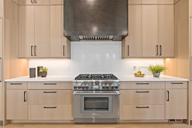 kitchen with light brown cabinetry, backsplash, wall chimney exhaust hood, and high end range