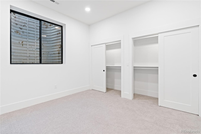 unfurnished bedroom featuring multiple closets and light colored carpet