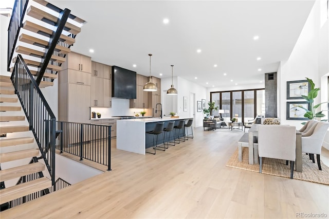 kitchen with an island with sink, light wood-type flooring, a kitchen bar, decorative light fixtures, and wall chimney range hood