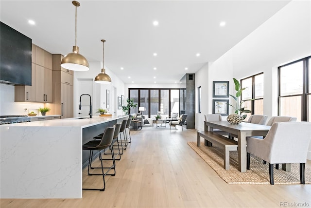 kitchen featuring gray cabinetry, light hardwood / wood-style floors, light stone counters, pendant lighting, and a kitchen bar