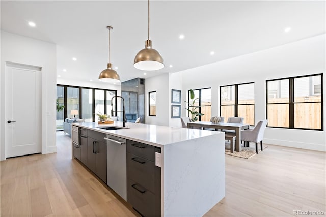 kitchen with light wood-type flooring, a healthy amount of sunlight, a kitchen island with sink, and pendant lighting