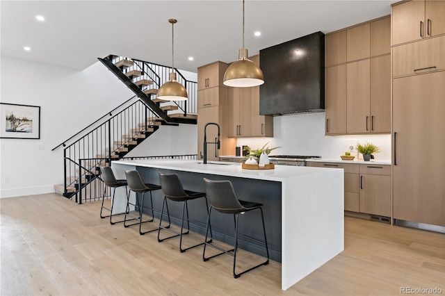 kitchen featuring a center island with sink, light brown cabinets, and exhaust hood