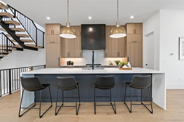 kitchen featuring ventilation hood, decorative light fixtures, a kitchen island with sink, and light hardwood / wood-style flooring