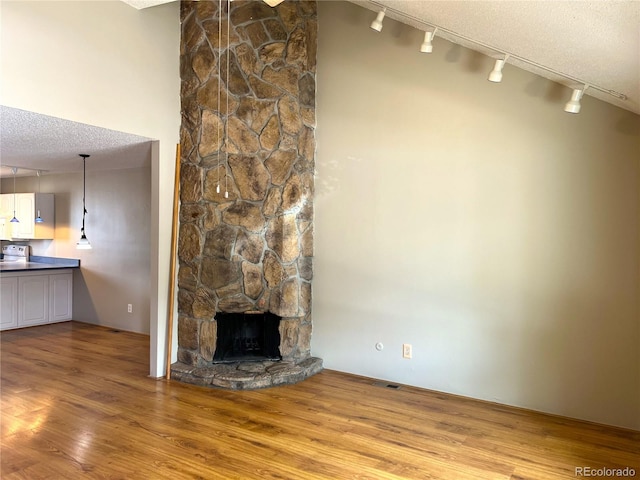 unfurnished living room with rail lighting, a textured ceiling, wood-type flooring, and a fireplace