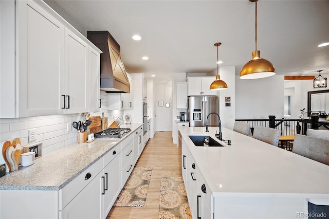 1485 Captiva Beach Ln, Monument, CO 80132 - kitchen with stainless steel appliances, custom exhaust hood, light wood-type flooring, an island with sink, and light countertops
