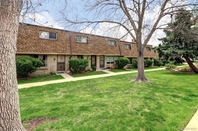 view of front of property with a shingled roof, mansard roof, brick siding, and a front yard