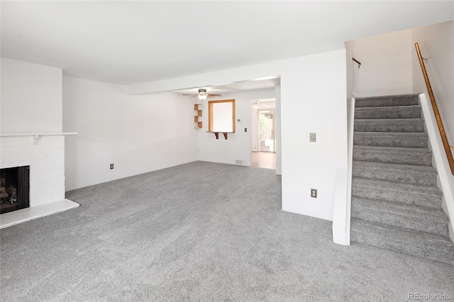unfurnished living room with carpet flooring, a ceiling fan, a brick fireplace, and stairs